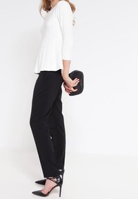 Haut blanc côtelé à manches trois-quarts, associé à un pantalon noir droit et des escarpins noirs à talons aiguilles. Tenant une petite pochette noire.