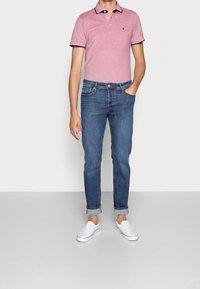 Rosa pikétröja med marinblå detaljer, ljusblå jeans och vita slip-on skor. Jeansens benslut är uppvikta, vilket ger en avslappnad passform.