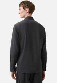 Donkergrijs shirt met lange mouwen, een puntige kraag, knoopsluitingen bij de mouwen en een soepele textuur. Beschikt over een strak, minimalistisch ontwerp en een getailleerde pasvorm.