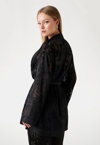 Czarny, przezroczysty kimono z kwiatowym wzorem, długimi rękawami i paskiem do związania. Gładka tekstura, elegancka sylwetka i kontrastowe satynowe wykończenie.