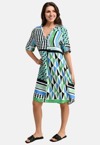 Musterkleid mit verschiedenen geometrischen Formen in Grün, Blau, Schwarz und Weiß. Kurzärmlig, V-Ausschnitt und knielange Gestaltung.