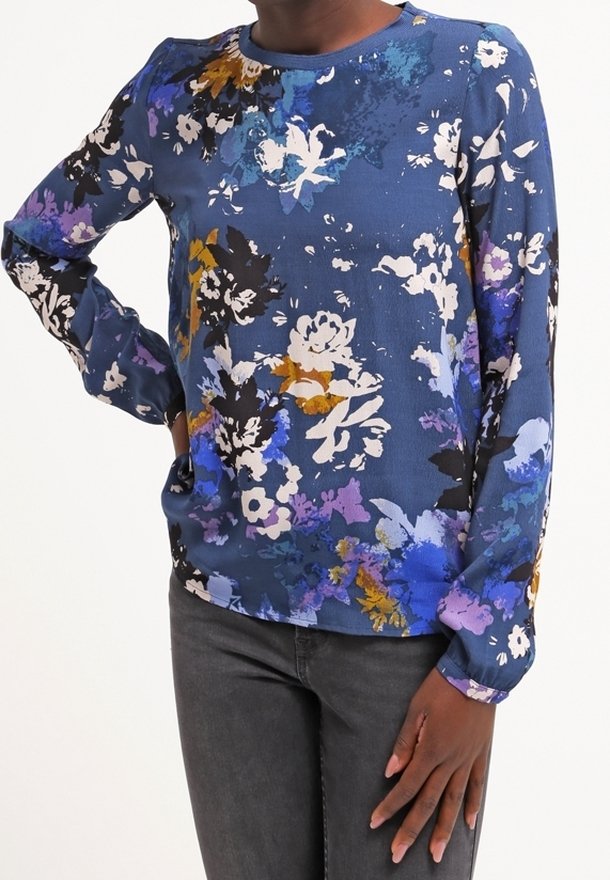 Långärmad blus i blått tyg med ett flerfärgat blommönster som har vita, gula och lila blommor. Rund halsringning, avslappnad passform.