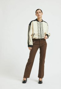 Bela bomber jakna s crnim akcentima, koja ima predni zip i dekorativno vezivanje, u kombinaciji s smešnim hlačama ravnog kroja i crnim potpeticama.