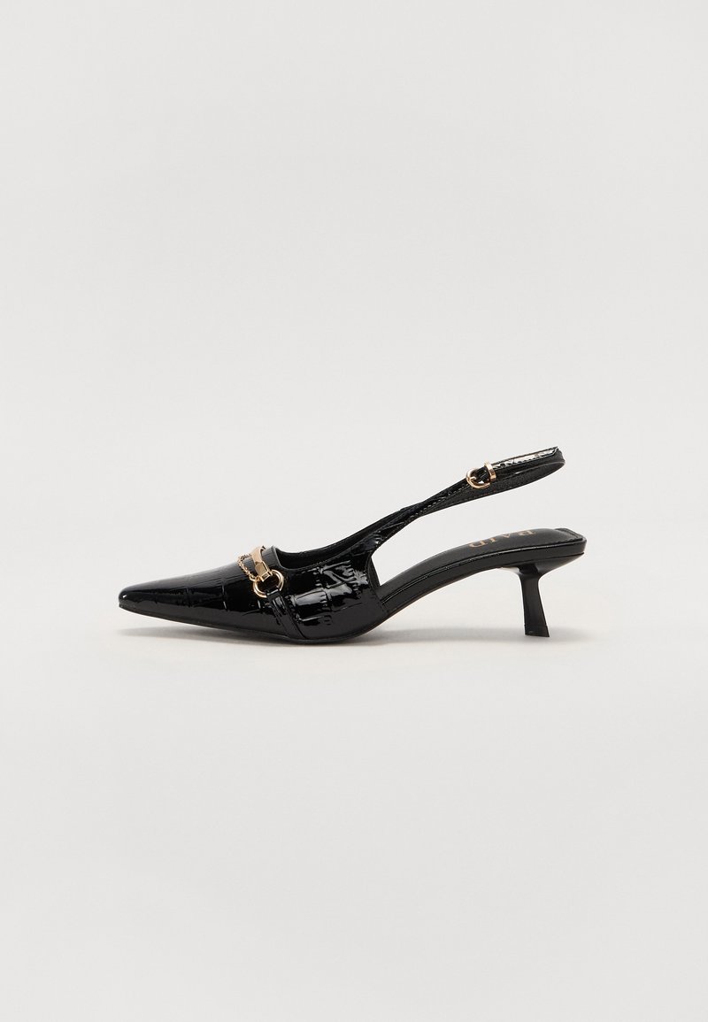 Escarpin slingback en cuir verni noir avec petit talon kitten, bout pointu et boucle dorée sur la bride avant, sur fond blanc.