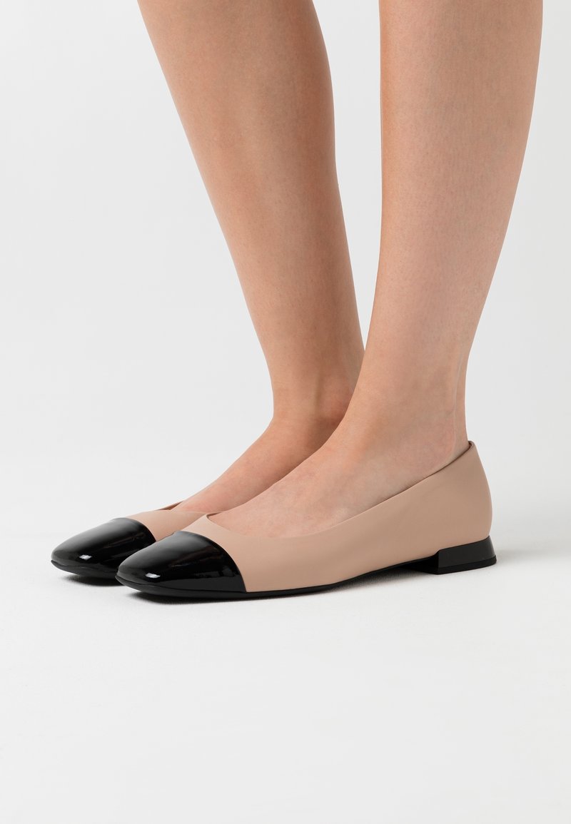 Beżowe baletki z czubkiem z czarnej lakierowanej skóry. Gładka tekstura, miękki materiał, niski obcas i minimalistyczne elementy designu.