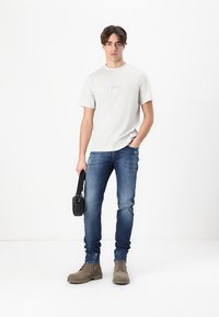 Ανοιχτό γκρι κοντομάνικο μπλουζάκι, μπλε τζιν παντελόνι, μπεζ μπότες και μαύρη τσάντα ώμου. Μινιμαλιστικός σχεδιασμός με διακριτική επωνυμία στην μπλούζα.