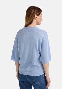 Pull en tricot bleu clair à manches courtes avec un col, offrant une coupe décontractée et un ourlet côtelé, mettant en valeur une texture douce.