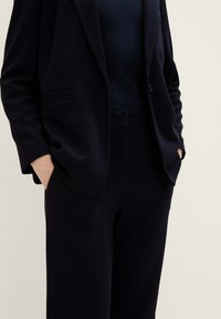 Donkerblauwe op maat gemaakte blazer van gestructureerde stof, met enkele knoopsluiting en zakken. Gecombineerd met bijpassende slim-fit broek.