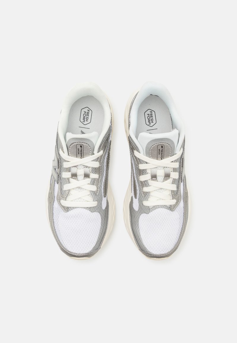Zapatillas deportivas gris y blancas con parte superior de malla, punta redonda, cordones blancos y suela blanda con la marca en la lengüeta.