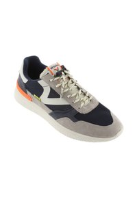 Sneaker con una parte superiore in suede e mesh grigio e blu navy, logo bianco, dettagli in suede grigio e un particolare arancione sul tallone. Suola di colore chiaro.