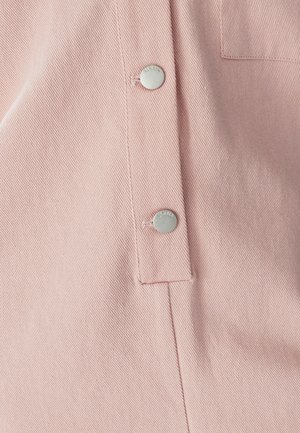 Šviesiai rožinės spalvos audinys su matoma tekstūruota pynimo raštą, matomi du sidabriniai metaliniai mygtukai. Viename mygtuke yra įspaustas tekstas. Minimalistinis dizainas.