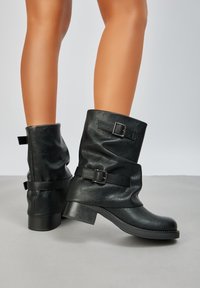Bottes noires en cuir à hauteur de cheville avec un design nonchalant, deux boucles ajustables, un petit talon et une surface texturée.