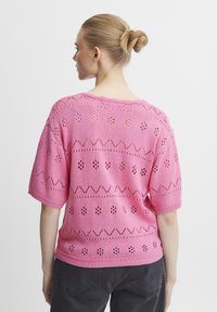 Ružový pletený sveter s krátkymi rukávmi, ktorý sa vyznačuje otvorenými vzormi a rebrovaným lemom. Zadná strana má vykrojený výstrih a štruktúrované detaily.