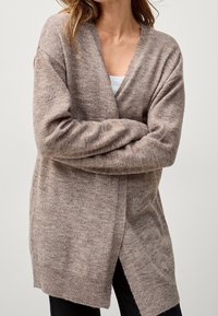 Jasnobrązowy kardigan z dekoltem w kształcie litery V, długimi rękawami i bocznymi rozcięciami. Wykonany z miękkiego, teksturowanego materiału, ma ściągacze na rękawach i u dołu.