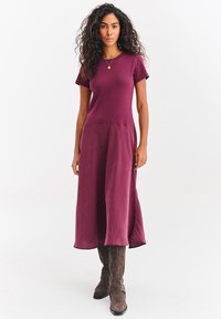 Bordowa sukienka midi z krótkimi rękawami, z dopasowanym gorsetem i luźną spódnicą. W zestawieniu z brązowymi zamszowymi kozakami za kolano.