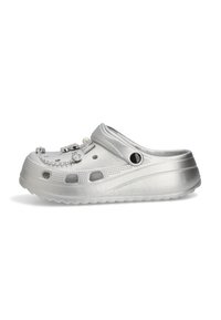 Zapato tipo clog en plata con agujeros de ventilación y adornos decorativos sujetos en la parte superior.