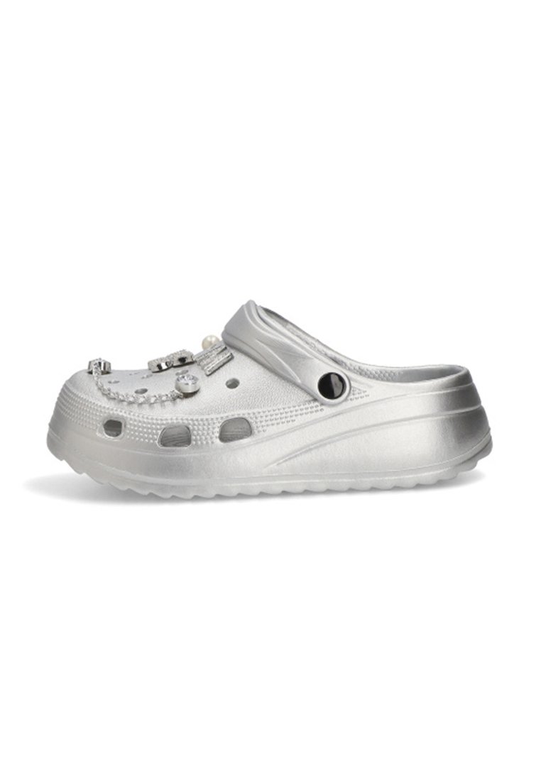 Zapato tipo clog en plata con agujeros de ventilación y adornos decorativos sujetos en la parte superior.