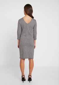 Grå och svart mönstrad klänning med V-ryg, trekvartsärmar, slim fit, knä-längd, tillsammans med svarta högklackade sandaler.