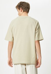 Beige rento t-paita, jossa on lyhyet hihat, raglan-saumat ja suora helma. Valmistettu pehmeästä puuvillamateriaalista, jossa on minimaalinen ommel.