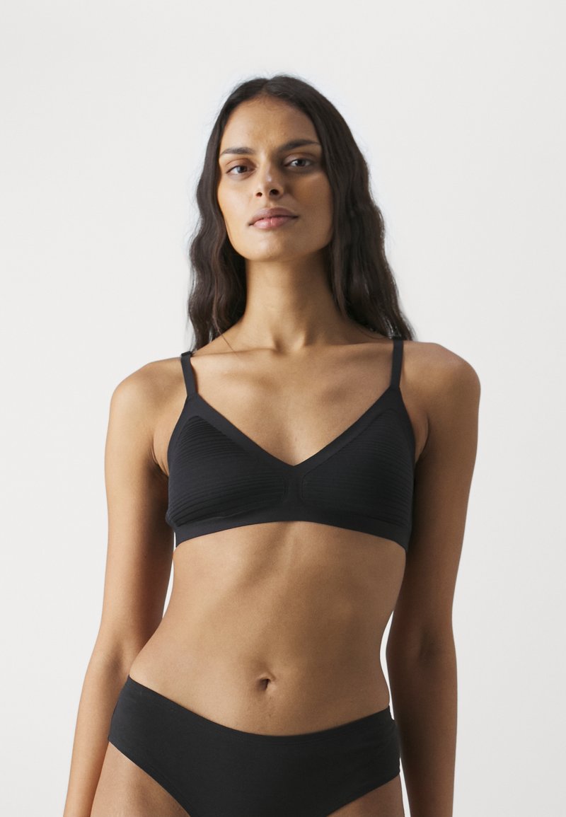 Soutien-gorge noir en tissu texturé avec un décolleté en V, de fines bretelles et sans rembourrage. Associé à un sous-vêtement noir assorti.