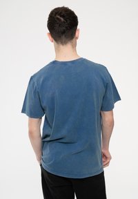 Short-sleeve, crew-neck t-shirt in faded blue cotton. Features a relaxed fit and stitched detailing along the neckline and sleeves.