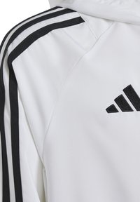 Witte sportjack met zwarte accenten en drie zwarte strepen langs de mouwen. Voorzien van een geborduurd zwart logo op de borst. Glad van structuur.
