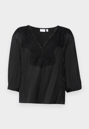 Černá blůza s výstřihem do V, která má složité černé krajkové zdobení kolem výstřihu a tříčtvrteční rukávy s elastickými manžetami.