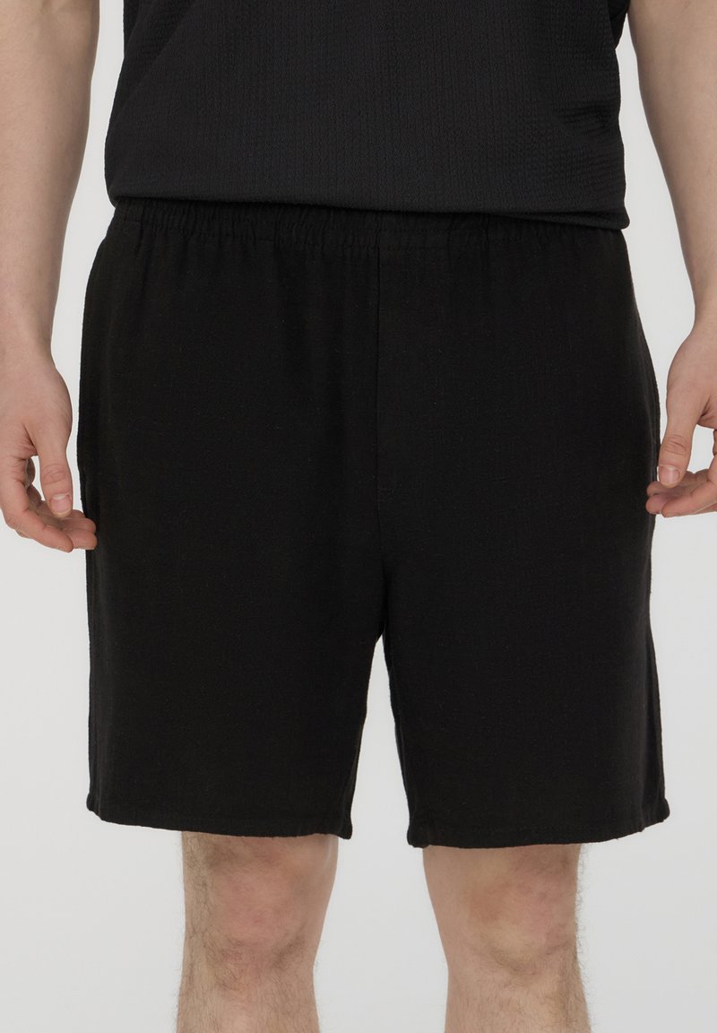Pantaloni shorts neri realizzati in un tessuto leggero, con una vita elasticizzata e un taglio dritto, privi di tasche o motivi visibili.