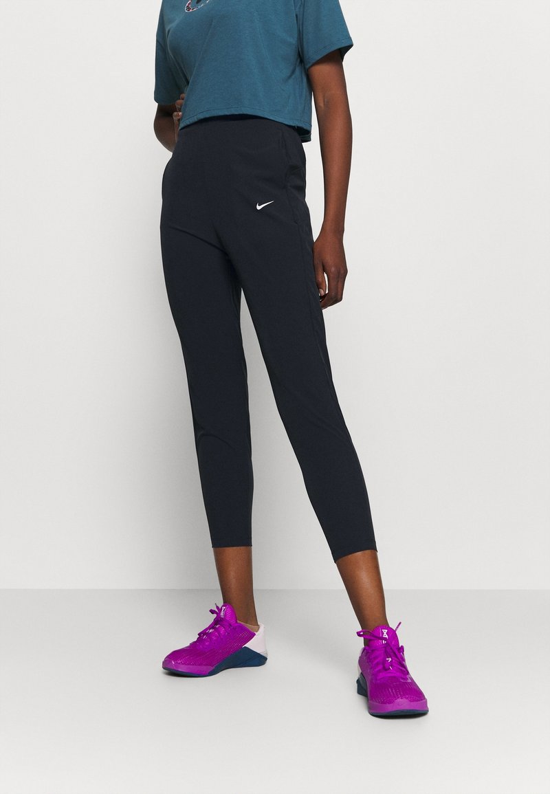 Zwarte leggings met een gestroomlijnde pasvorm, gecombineerd met een teal cropped T-shirt met een ronde halslijn en een grafische print. Heldere paarse sportschoenen.