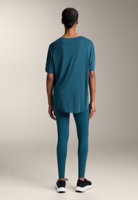 Teal színű sportpóló, rövid ujjal és kerekített hemével, melyhez illő teal színű leggings tartozik, szögletes varrásmintával. Fekete tornacipők.