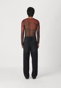 Long-sleeve mesh top in dark red, semi-transparent with a fitted silhouette, paired with loose, black denim pants featuring back pockets.