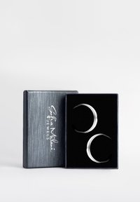 Orecchini a cerchio in tono argento con forma a mezzaluna, presentati in una scatola blu scuro con un interno nero morbido e il testo del logo.