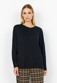 Svart långärmad topp i mjukt tyg, med rund hals och avslappnad passform, kombinerad med mönstrade beige byxor.