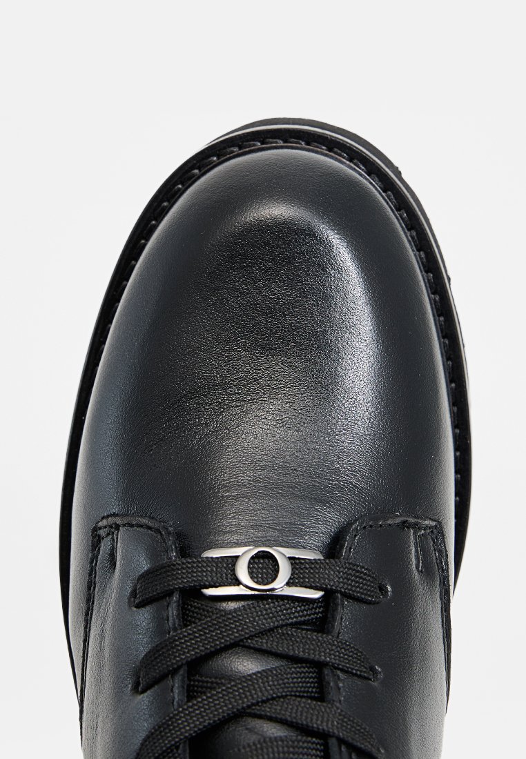 Zwarte leren schoen met een gladde textuur, ronde vorm en platte zolen. Heeft zwarte veters en een zilveren oogje accent nabij de veters.