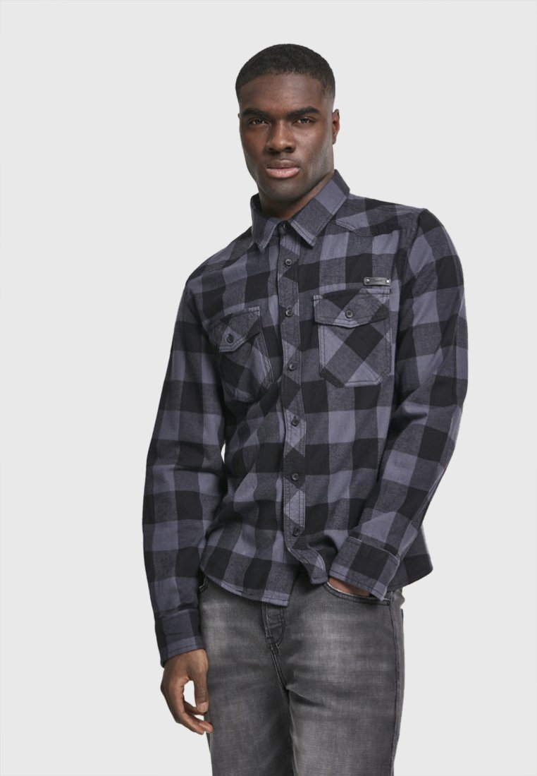 Camisa de franela a cuadros en negro y gris, con mangas largas, dos bolsillos en el pecho y cierre de botones. Combinada con jeans de mezclilla grises.