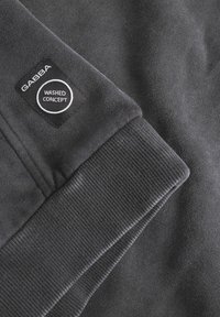 Dark gray sweatshirt featuring a ribbed cuff and a black label with "GABBA" and "WASHED CONCEPT" text in white circular design. Soft texture.