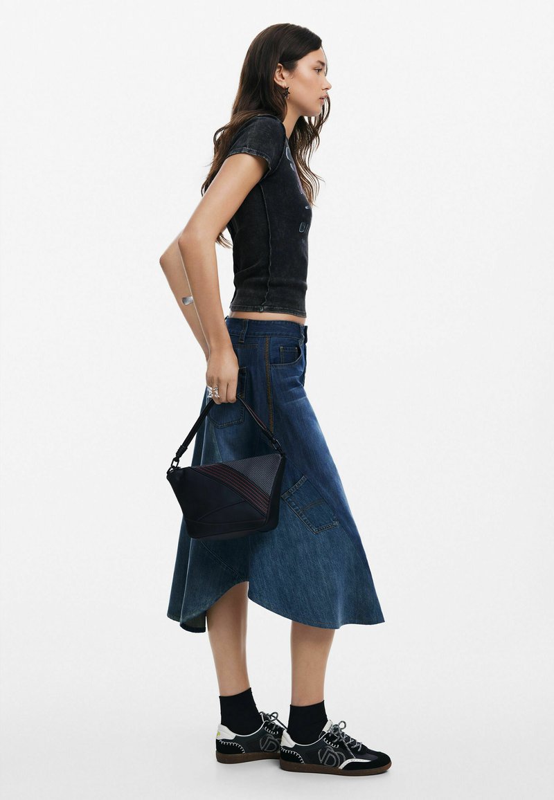 Camiseta negra ajustada, falda larga de mezclilla azul, bolso cruzado negro con detalles rojos, zapatillas negro y blanco con un diseño deportivo.