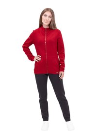 Giacca rossa con zip e colletto alto, due tasche frontali e maniche lunghe, abbinata a pantaloni neri e sneakers bianche. Tessuto dalla texture liscia.