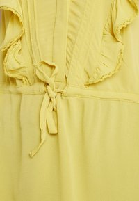 Tissu jaune avec un volant le long de la couture et un nœud noué à la taille sur un vêtement doux et texturé.
