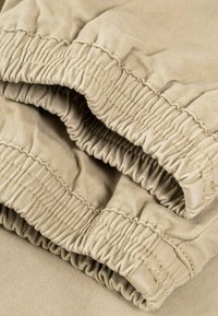 Tela beige con primer plano de los puños elásticos fruncidos, mostrando la costura y la textura del material tejido.