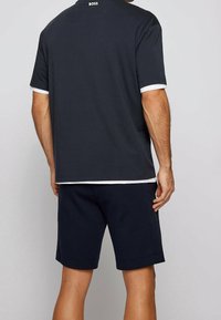 Marinblå polo skjorta med vita detaljer, oversized passform, korta ärmar och logotyp på ryggen, ihop med matchande marinblå shorts. Avslappnad tygtextur.