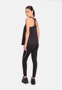 Melna sporta topiņš ar racerback dizainu, saskaņots ar melniem pieguļošiem legingiem ar baltu sānu svītru un masīviem melniem sporta apaviem.