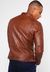Chaqueta de cuero marrón estilo biker con un diseño ajustado, detalles de costura visibles y un corte hasta la cintura. Forrada con cremalleras en los bolsillos.
