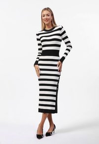 Robe en maille rayée noir et blanc avec une silhouette ajustée, des manches longues, un col rond et des boutons le long du côté gauche.