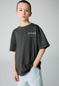 Anglies pilkos spalvos trumpas rankovėmis marškinėliai su mėlynu "ALLSAINTS" logotipu, laisvas kirpimas, minkšta medvilnė ir apvalia iškirpte. Dėvimi su šviesiais džinsais.