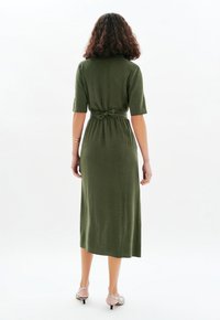 Robe verte olive, longueur genou, à manches courtes et taille ajustée nouée avec un nœud. Fabriquée en tissu texturé, elle présente une silhouette droite.