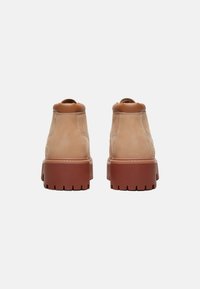 Stivali alla caviglia in pelle beige con suola in gomma marrone, design minimalista, punta rotonda e dettagli cuciti al collo e sul retro.