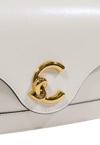 Hvid lædertaske med klap og en skinnende, guldfarvet metalspænde formet som et stiliseret bogstav "C".