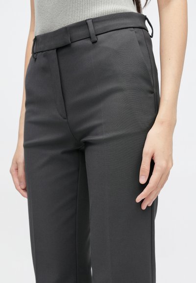 Hallid hallid püksid siledast materjalist, millel on vööaukude, eesmine tasku ja kitsas lõike disain. Nähtav käsi lebab kergelt reie peal.