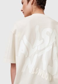 Camiseta de gran tamaño color crema hecha de algodón, con grandes letras texturizadas en blanco en la parte posterior que dicen "ALLSAINTS LONDON."